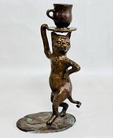 Front view of bronze cat candleholder showing the cup and saucer held above the cat's head, standing on an oval base.