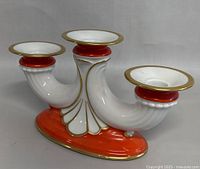 Front left angle view of the three-light candlestick showing details of the white porcelain, gold trim, and red accents on the base and rim.
