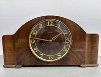 Front view of the wooden mantel clock with visible dial, gold numerals, and hands, showcasing the curved Art Deco style case.