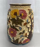Front view of vintage ceramic vase with floral and branch relief design in colors pink, yellow, blue, green and brown on cream background.