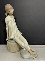Front angle showing the face and upper body of the girl figurine in porcelain, seated on a cushioned stool with a relaxed pose.