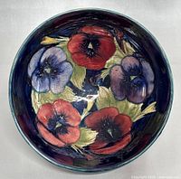 Top view of the pottery bowl showing detailed floral design with red and purple pansy flowers and green leaves on deep blue background.