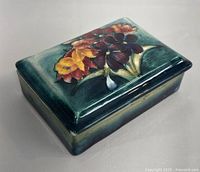 Closed view of the rectangular box showing the floral painted lid in various colors on green background.