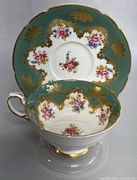 Front view of teacup inside saucer showing floral and gold scroll design with green border.