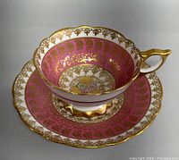 Photo showing the teacup resting on the saucer, displaying pink and gold floral pattern with gold trim and gold-painted handle.