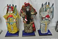 Three Chinese opera dolls standing on blue bases, showing front view of detailed embroidered costumes and headdresses.