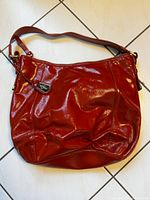Front view of the red patent leather shoulder bag with Cole Haan logo plaque and strap.