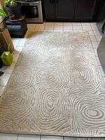 Full view of cream-colored area rug on tile floor showcasing overall woodgrain-inspired pattern and size