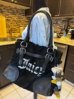 Full side view of black Juicy Couture velour tote bag with leather trim, silver-tone buckles, embroidered logo, and attached multi-color tassel charm