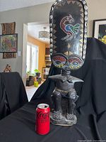 Full front view of the Zulu fertility doll statue with soda can for size scale. Seated female figure carved from wood with dark patina and detailed beadwork on head and waist, cowrie shells around head.