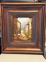 Front view of the entire framed oil painting depicting a European village scene with cobblestone street and waterfront view.