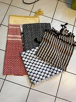 Four Middle Eastern keffiyeh scarves laid out on tiled floor showing various patterns and tassels.
