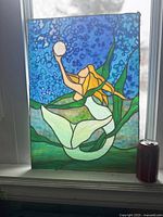 Full stained glass panel showing mermaid holding pearl with blue ocean background and green seaweed, with metal frame and soda can for size reference.