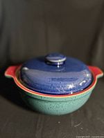 Side view of the covered casserole baking dish showing blue lid with knob handle and teal speckled body with red trim on rim and handles.