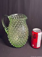 Front angle view of green hobnail glass pitcher next to soda can for size reference.