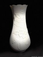 Front side view of bisque porcelain vase showing raised floral relief pattern and scalloped rim.