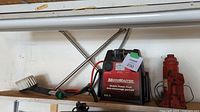 Shelf with the MotoMaster mobile power pack jump starter, scrub brush, and red bottle jack.