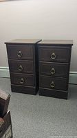 Front view of two matching wooden bedside tables, each with three drawers and brass ring pulls.