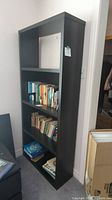 Front angle view of black bookshelf with books on shelves, showing overall design and condition.