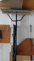 Large push broom with wide gray bristle head mounted vertically, black handle visible