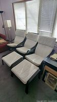 Three armchairs with black wooden frames and white cushions and two foot stools with matching black frames and white cushioned tops. Cushions have staining.