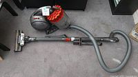 Overview of the canister vacuum body, flexible hose, wand and floor head laid out on carpet