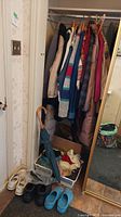 Closet with coats and multiple pairs of shoes and umbrellas on the floor