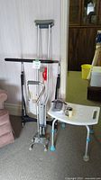 Shows pair of aluminum crutches, black bed rail, white shower seat, and small mobility aids.