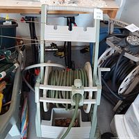 Front view of green garden hose coiled on cream and green Ames Reel Easy hose caddy showing wheels and handle