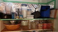 Shelf with Mason jars, plastic containers, wooden and metal salad bowls, soft coolers, and food warmer
