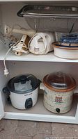 Shelving with kitchen appliances and utensils including hand blender, immersion blender, sieve, glass bowl, and ceramic dishes