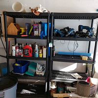 Front view of two black plastic shelving units filled with various workshop and household items, showing details and condition of shelves.