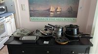 Front view of the assortment of pots and pans displayed on a black cabinet with a nautical themed poster behind them.