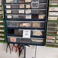 Full view of wall-mounted organizers showing labeled drawers with various small fasteners and nails with hand tools hanging below