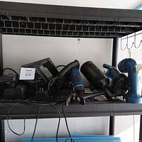 A set of power tools on a shelf, including a belt sander with Black & Decker label, a drill, a flashlight, a jigsaw, and a circular saw, with cords visible.