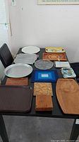 Overview of various trays, platters and cutting boards with different materials including wood, metal, glass, ceramic, and fabric, arranged on a table.
