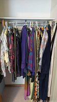 Wide shot of the closet rod showing multiple clothing items on hangers including dresses, coats, and shirts in various colors and styles.