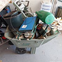 Wide angle of wheelbarrow filled with assorted garden tools, pots and decorations showing overall contents and condition.