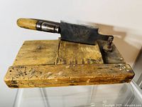Photo showing entire wooden tobacco cutting board with large iron cleaver blade mounted and hinged at one end, with visible wood grain and patina.