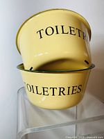 Two stacked yellow enamel bowls labeled 'TOILETRIES' with green rims, showing minor wear.