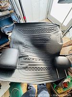 Rear black rubber cargo mat with textured design and 'EXPLORER' logo, alongside two leather headrests on top, displayed on floor near door.