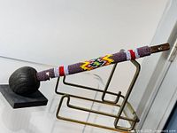 Side view of the Kerrie wooden stick showing carved round knob, beaded shaft with multicolor geometric pattern, and natural wood handle end.