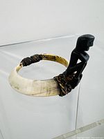 Photo showing side view of the rattan armband with attached dark carved wood figurine, highlighting woven binding and natural color variations in rattan.