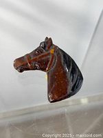 Close-up image of the brown and black painted carved horse head brooch showing details of the horse's eye, ear, and bridle.