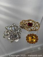 Three vintage brooches including clear rhinestone cluster, gold-tone filigree with red and clear glass stones, and amber yellow glass stone brooch