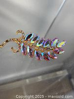 Photo showing whole brooch on clear acrylic display highlighting the gold tone setting and iridescent marquise rhinestones arranged as leaves.