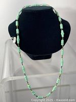 Full view of vintage green glass bead necklace on black bust display, showing bead arrangement and length.