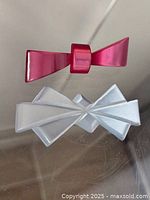 Pink and white Lucite bow brooch pins displayed on clear surface, showing general shapes and condition of both pieces.