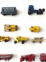 Top-down view of assorted vintage toy trucks including box trucks, yellow construction vehicles, and red farm machinery on white background.