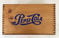 Top view of wooden Pepsi-Cola crate lid showing large blue logo and natural wood grain.